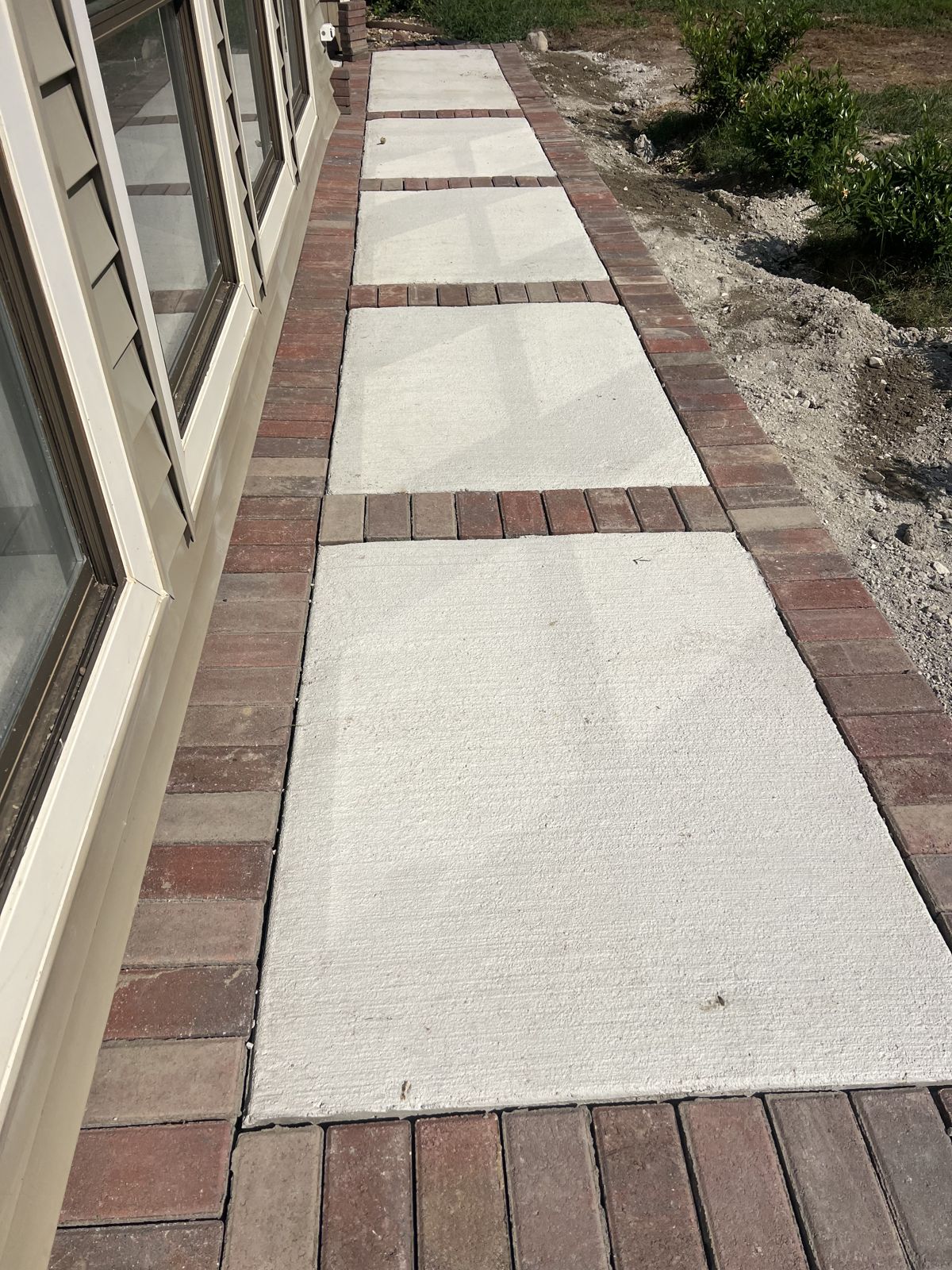 Paver-bordered concrete walkway running along the side of a home